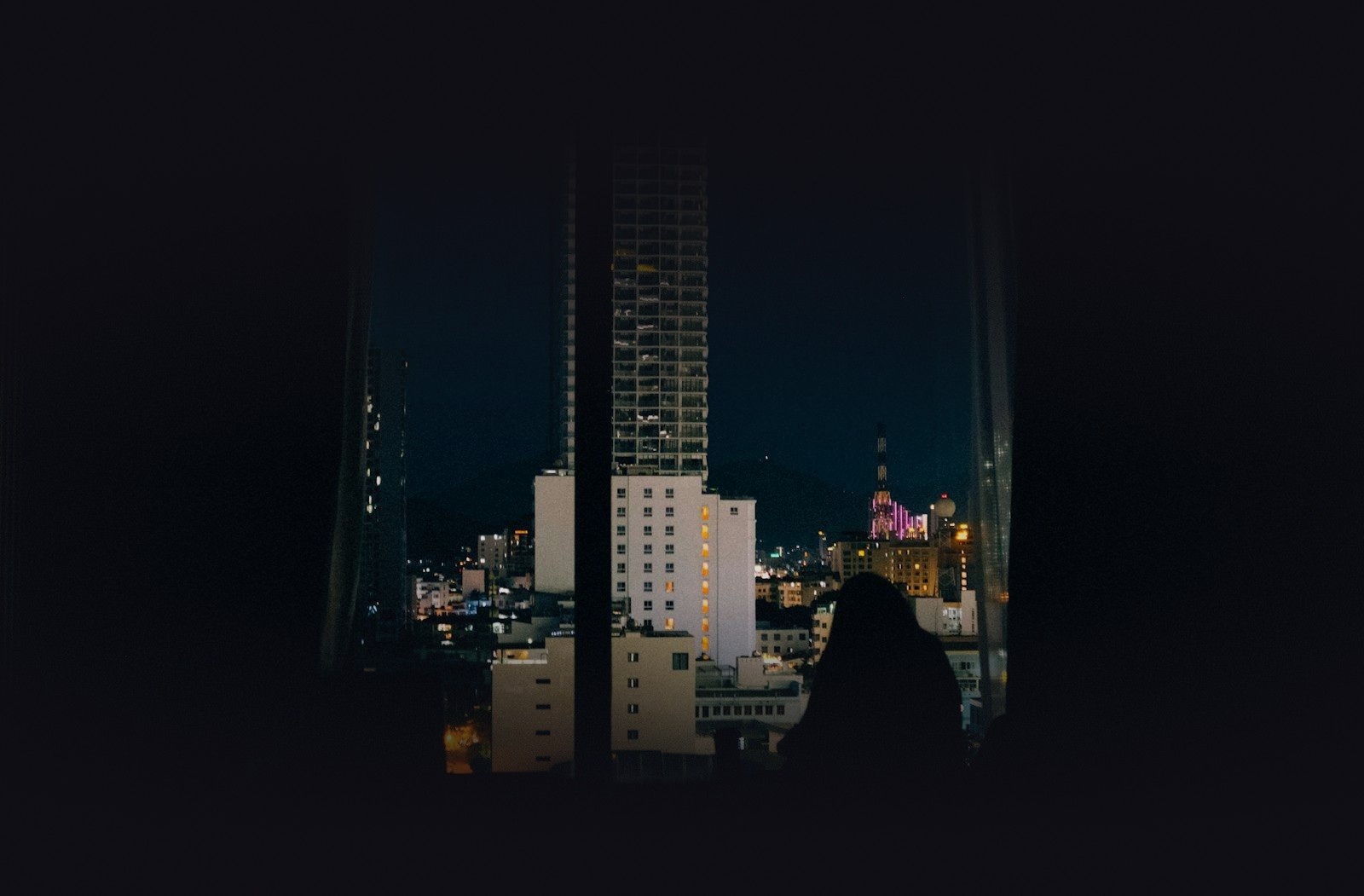 A silhouetted figure working at a window over the night city