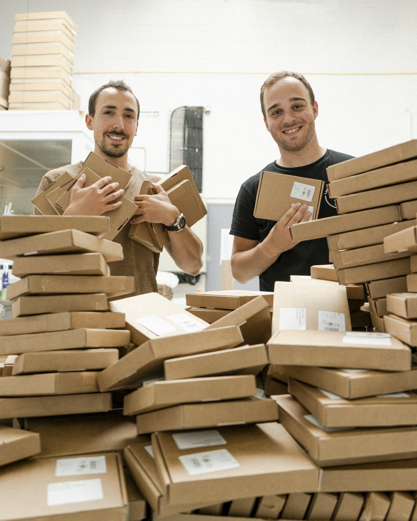 Two founders grinning behind a mountain of packed order boxes